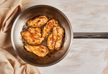 Chicken breast cooking in stainless steel pan