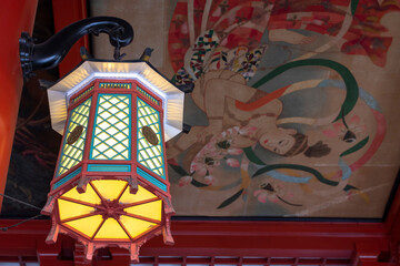 Lantern hanging from a Buddhist temple ceiling with the goddess painting in the background