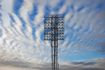 Spotlights on a lighting mast over the stadium against the blue sky with white clouds on a day