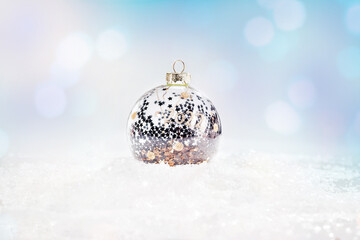 Shiny, silver glass Christmas ball on snow on a light background. Glittering,Shiny background.Christmas, winter, new year concept.copy space.Winter Background.Xmas and New Year holiday, bokeh, light