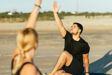Obraz premium Man raisin arm while doing a yoga next to his coach on the beach
