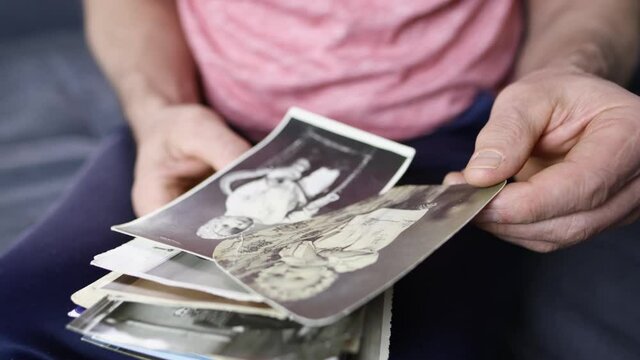 close-up of old male hands holding retro family photos of 1960-1965, vintage monochrome photographs in sepia color, genealogy concept, ancestral memory, family ties, childhood memories
