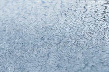 An abstract photo of a pattern of frost on a piece of glass.  The macro is a black and white textured frosty crystal snowflake. The unique patterns of silver ice crystals frosted the clear glass.