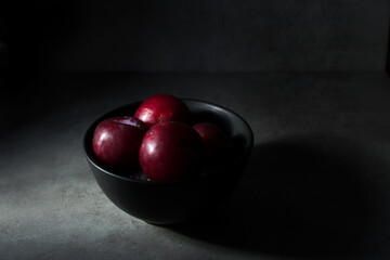 Darkfood style scene with a couple of fresh red plums in a black basket