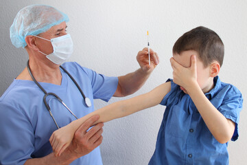male doctor, nurse in blue uniform makes an injection with a syringe to boy 8-10 years old, close-up hand of child, medical concept, vaccination against the covid-19 virus