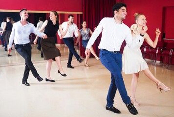 Happy young dancing couples enjoying active boogie-woogie in modern studio