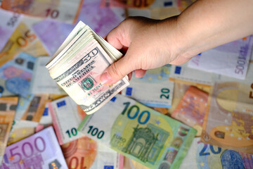 closeup female hands hold american money, count dollars against background of paper euro banknotes,...