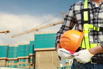 close up of construction worker carrying safety helmet with crane in the background and new...
