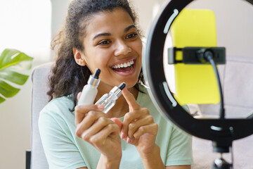 Young smiling African American beauty blogger or influencer holding serum bottle communication with...
