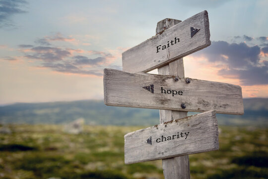 faith hope charity text quote on wooden signpost outdoors in nature during sunset.