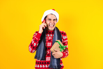 Portrait of Latin man holding Christmas gift box and calling by mobile phone on a yellow background in Mexico latin america