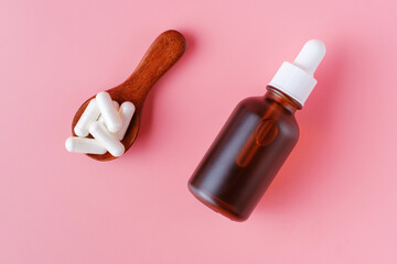 Capsules on wooden spoons and bottle with collagen on pink background.