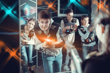 Fototapeta na wymiar Portrait of happy young man with laser pistol and playing laser tag with his friends in dark room. High quality photo