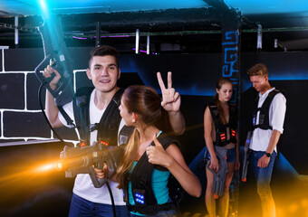 Fototapeta na wymiar young positive guy and girl are happy with their victory in laser tag game in dark laser tag room