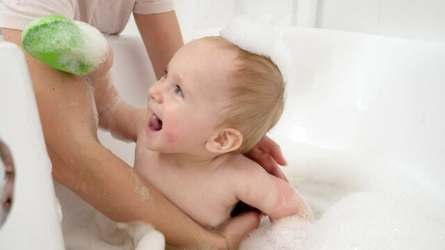 Funny baby boy with soap foam on head playing in bathroom with toy boats and ships. Concept of children hygiene, healthcare and development at home