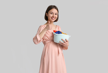 Young pregnant woman holding basket with baby clothes on light background