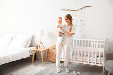 Young mother holding her cute little baby near crib in bedroom
