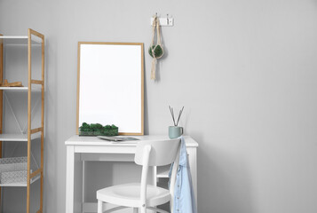 Modern workplace with big blank frame near light wall