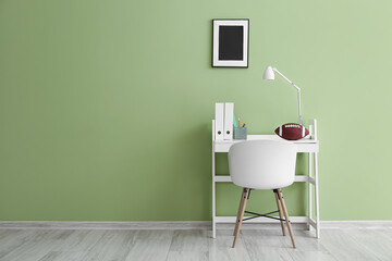 Modern workplace with folders and rugby ball near green wall