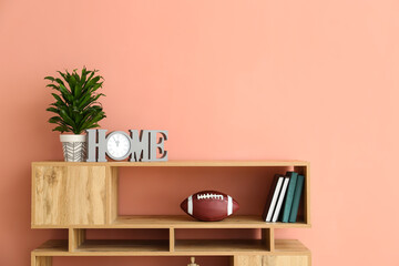Shelving unit with rugby ball, books and decor near pink wall