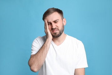 Young man suffering from headache on light blue background