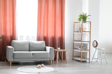 Interior of light living room with grey sofa, shelving unit and red curtains