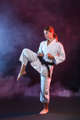 Obraz na płótnie Canvas Young woman practicing karate on dark background