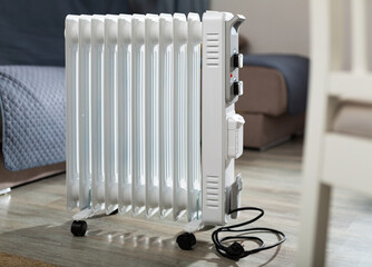 White metal portable oil heater standing in home room. Electric appliance for heating house..