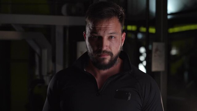 Front view close up portrait of one confident adult caucasian man male athlete with beard standing in dark gym looking to the camera nervous wearing black suit power of will and determination concept