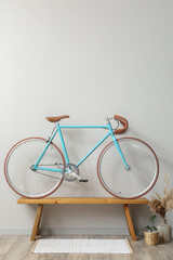 Modern bicycle on wooden bench near light wall