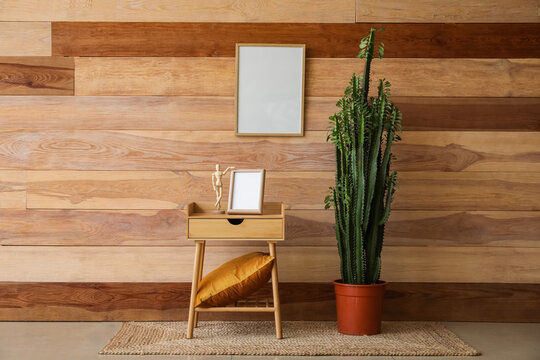 Green cactus, table with frame and mannequin near wooden wall