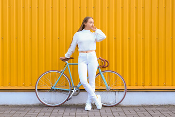 Pretty teenage girl with bicycle near yellow fence