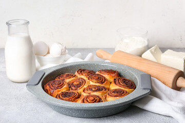 Baking dish with tasty cinnamon rolls on light background