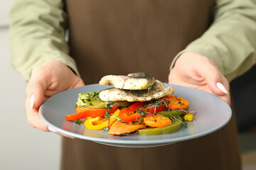 Woman holding plate of tasty sea bass fish with vegetables indoors, closeup