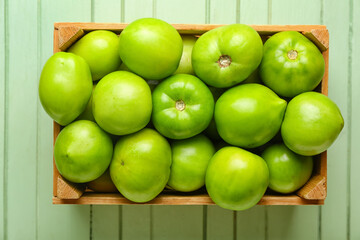Box with fresh green tomatoes on color wooden background