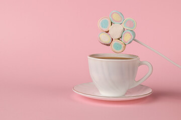 A set of colorful marshmallows on a stick over a cup of coffee on a pink background. The concept of a fun breakfast.