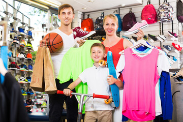 portrait of a positive young family of three picking various clothing in sport department