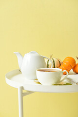 Tea pot, cup of hot beverage and pumpkins on table near yellow wall