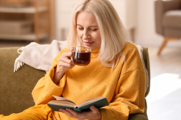 Beautiful mature woman reading book and drinking tea at home on autumn day