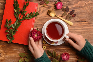 Female hands with cup of tea, notebook and aster flowers on wooden background, closeup