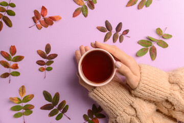 Female hands with cup of tea and autumn leaves on color background, closeup