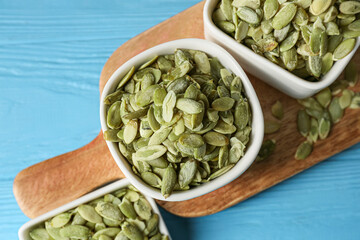 Bowls with pumpkin seeds on blue wooden background, closeup
