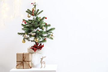 Small Christmas tree with gift on table near light wall