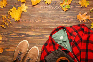 Stylish plaid jacket, shirt, pants, belt, shoes and autumn leaves on wooden background