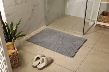 Soft grey bath mat and slippers on floor in bathroom - obrazy, fototapety, plakaty