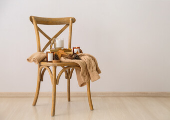 Burning candles in holders on chair, books and autumn leaves on chair near white wall