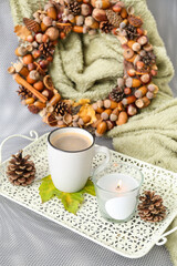 Tray with burning candle in holder, autumn decor and cup of coffee on armchair