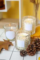 Burning candles in holders and autumn decor on table in room