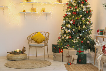 Christmas tree, gift boxes and chair near light wall in decorated room