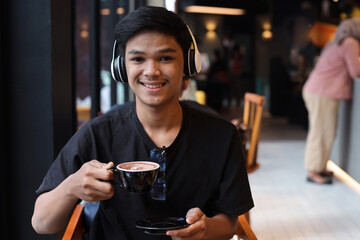 Asian male student drink a cup of coffee at the cafe and smiling to camera
